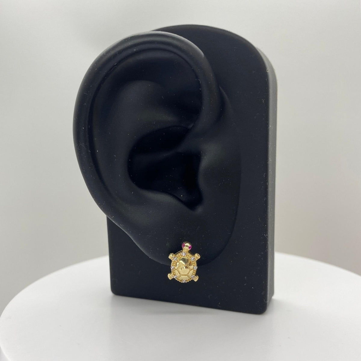 Small 10k gold turtle stud earring displayed on a black mannequin ear jewelry stand.
