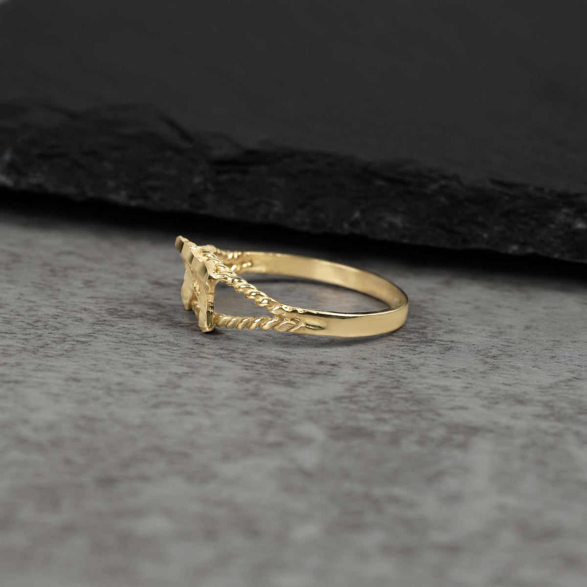 Side view of a 10k gold mini Uzi gun ring on gray stone.