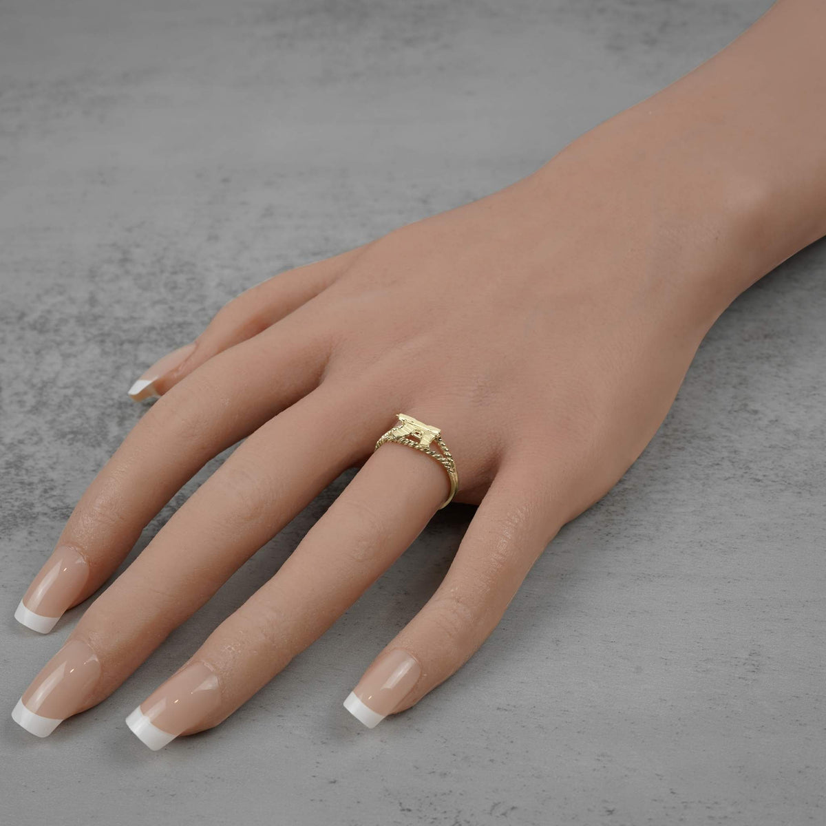 Model hand wearing a 10k gold mini Uzi gun ring on gray background.