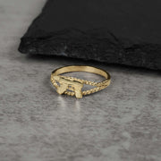 10k gold mini Uzi gun ring with a rope-textured band on gray stone.
