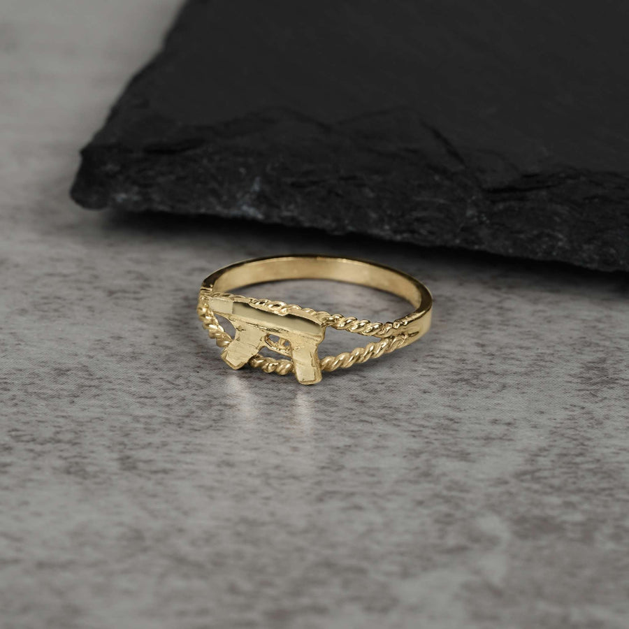 10k gold mini Uzi gun ring with a rope-textured band on gray stone.
