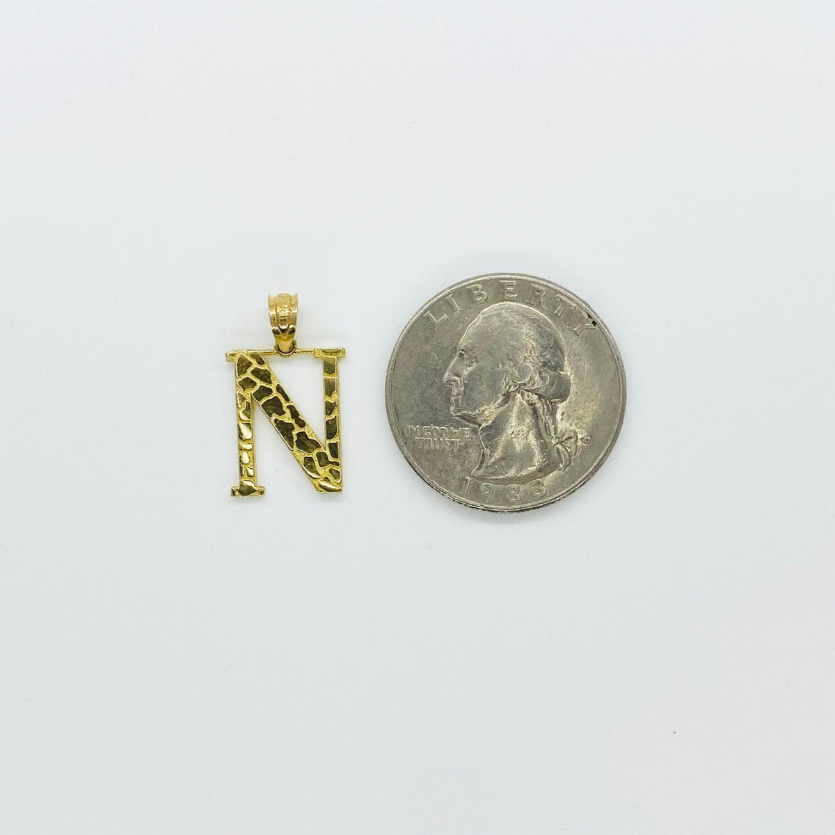 Size comparison of 10k gold nugget initial N pendant beside a US quarter coin.