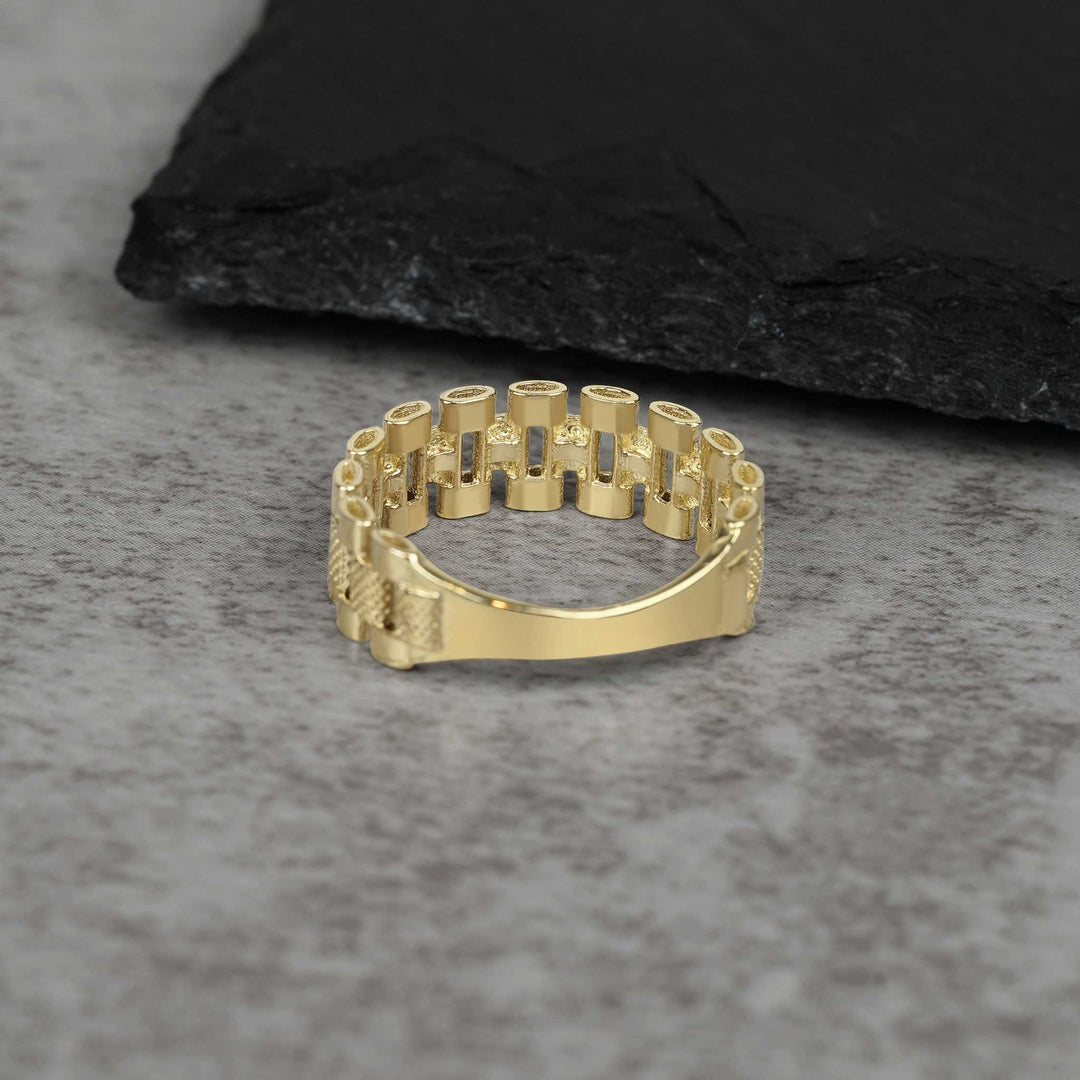 A single textured gold watch-link band ring on a grey stone surface.
