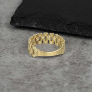 A single textured gold watch-link band ring on a grey stone surface.
