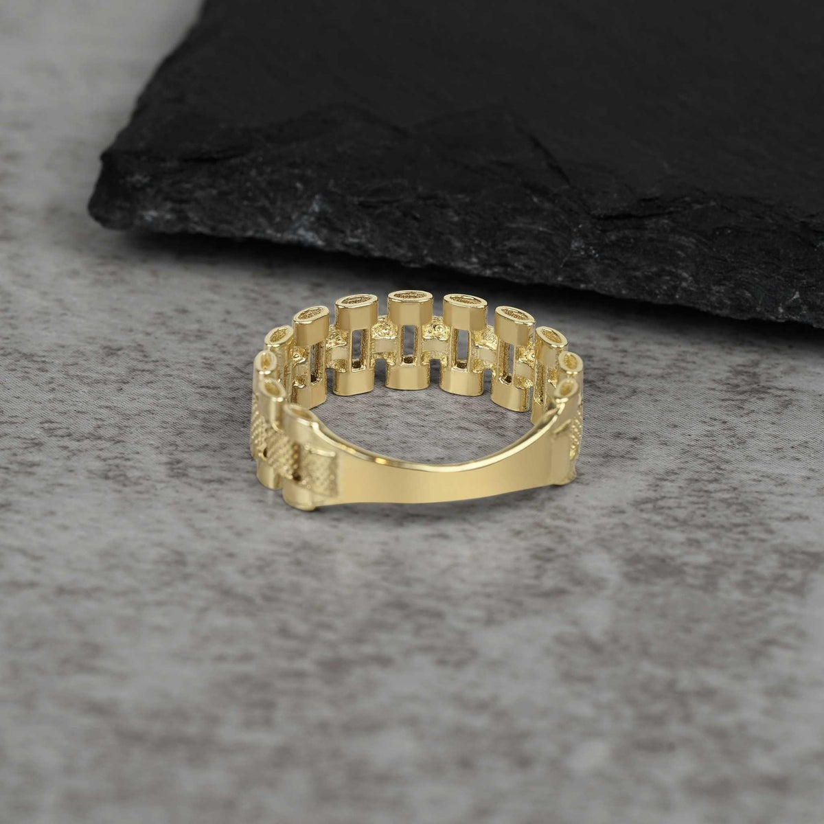 A single textured gold watch-link band ring on a grey stone surface.