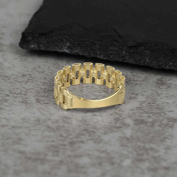A single textured gold watch-link band ring on a grey stone surface.
