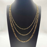 Three gold Figaro chain necklaces of varying widths layered on a black jewelry bust.