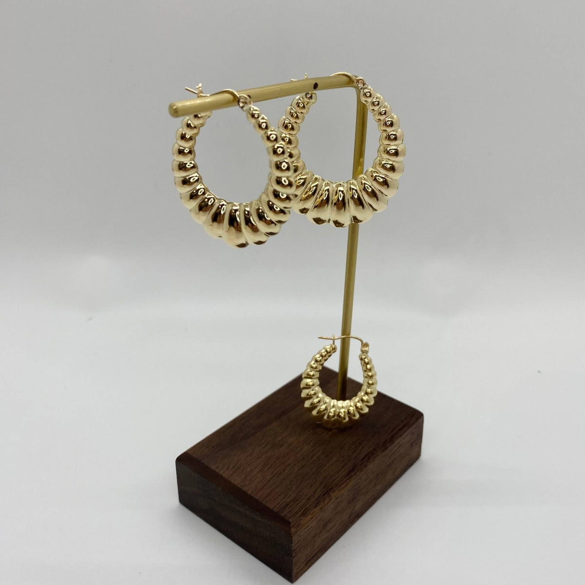 Pair of polished 10k yellow gold shrimp hoop earrings displayed on a gold stand.
