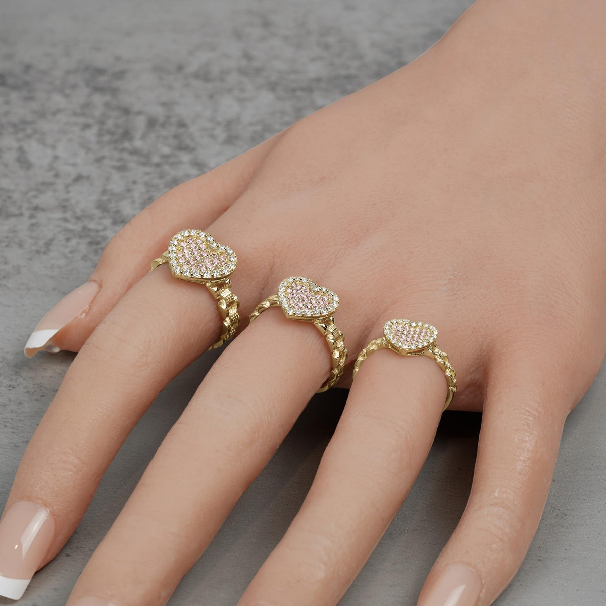Hand wearing three 10k gold heart-shaped rings with sparkling cubic zirconia stones.