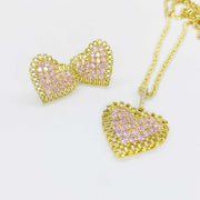 Gold heart pendant necklace and matching stud earrings with pink stones on white background.