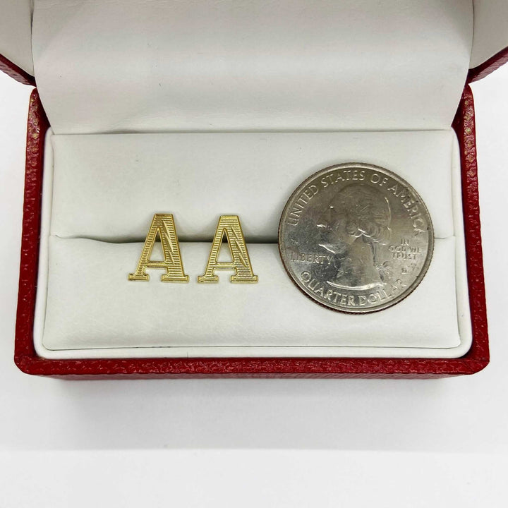 Pair of gold diamond-cut initial letter 'A' stud earrings displayed next to a quarter.