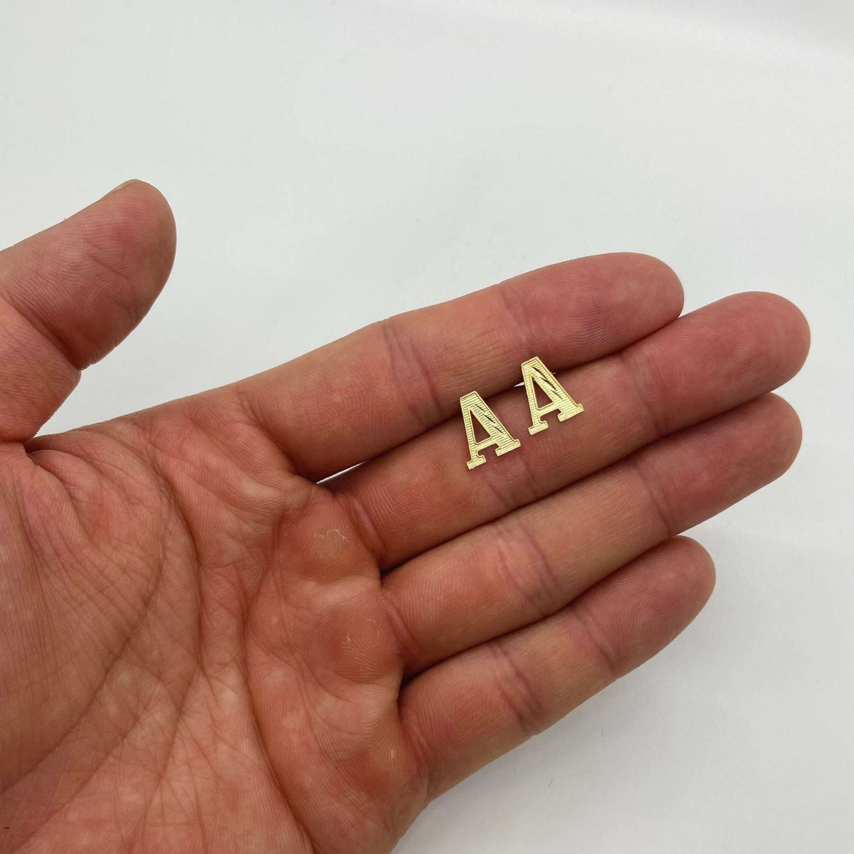 Pair of gold initial letter 'A' stud earrings held flat on an open palm.
