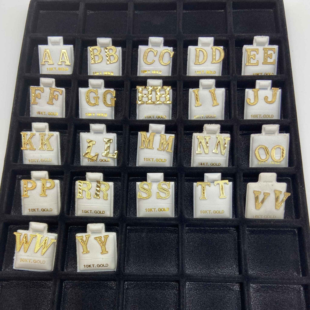 Full inventory display tray containing multiple pairs of gold diamond-cut initial letter stud earrings from A to Y.