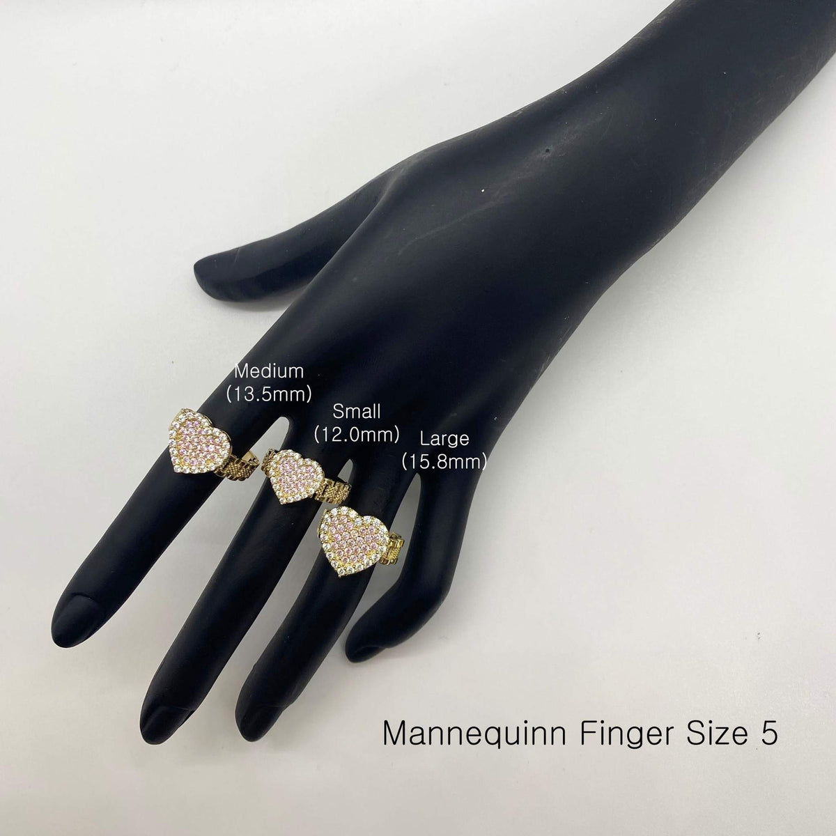 Three heart-shaped rings on a black mannequin hand with size labels.