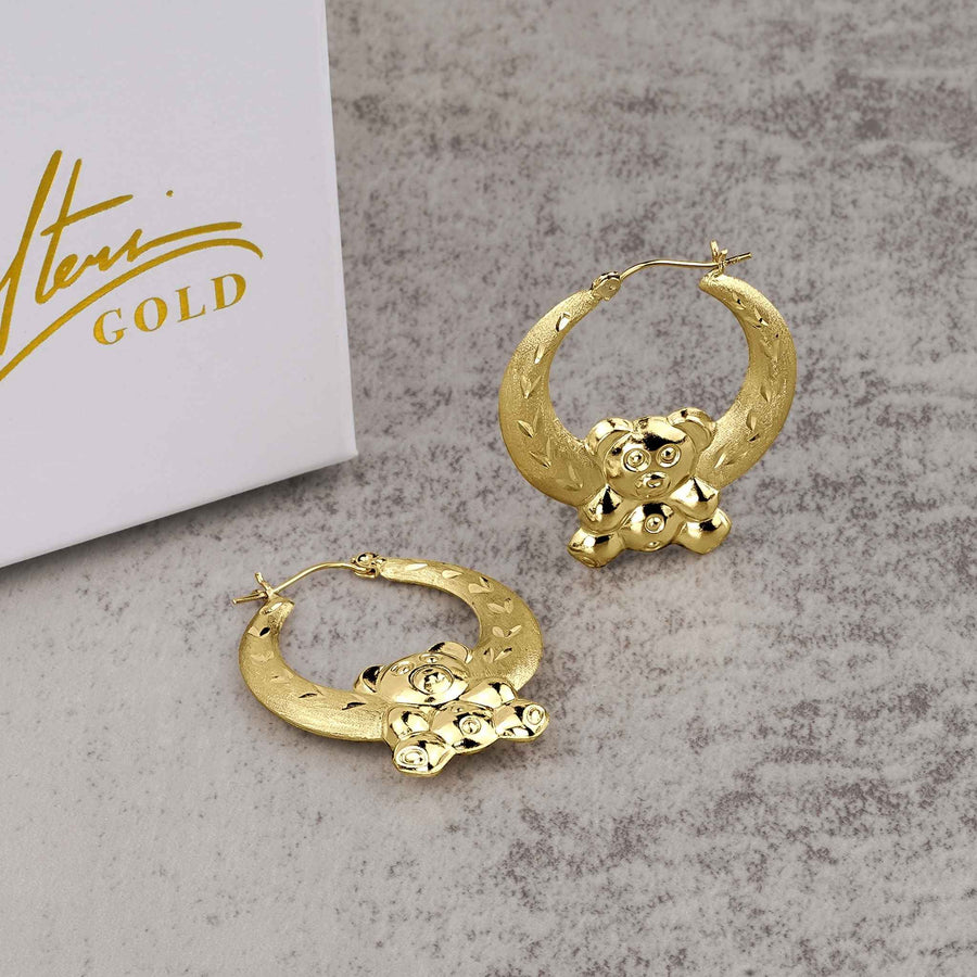 Pair of 10k yellow gold teddy bear-shaped hoop earrings resting beside a Nolters jewelry box.
