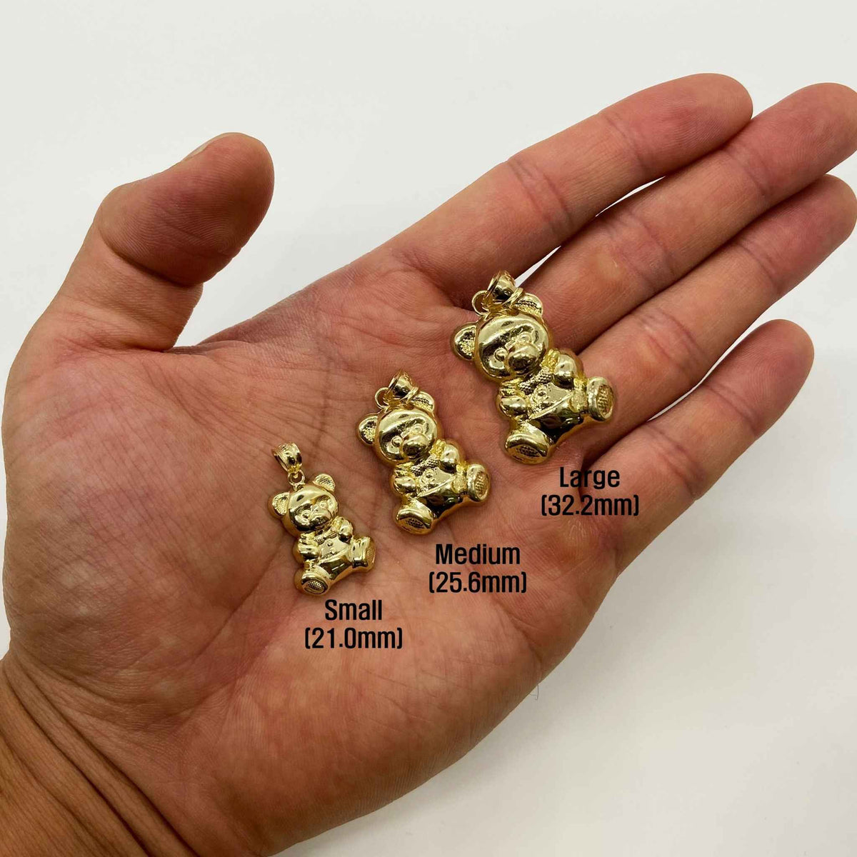 Small, medium, and large 10k gold teddy bear pendants displayed in a hand.