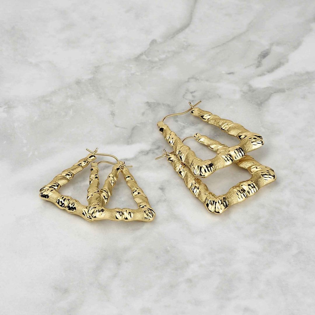 Two 10k gold twisted square hoop earrings with diamond-cut texture on a marble background.