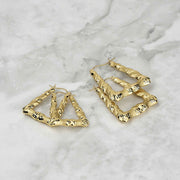 Two 10k gold twisted square hoop earrings with diamond-cut texture on a marble background.