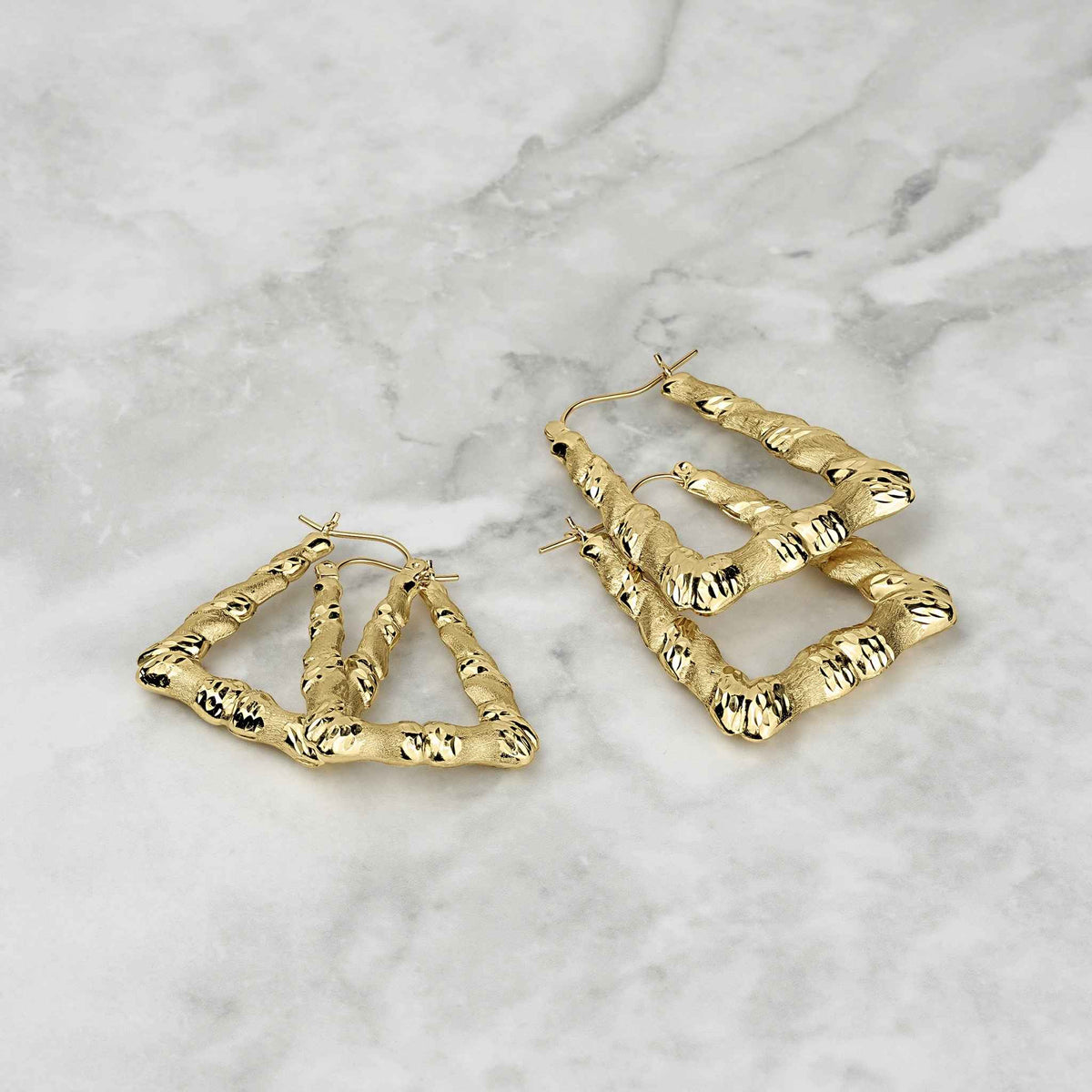 Two 10k gold twisted square hoop earrings with diamond-cut texture on a marble background.