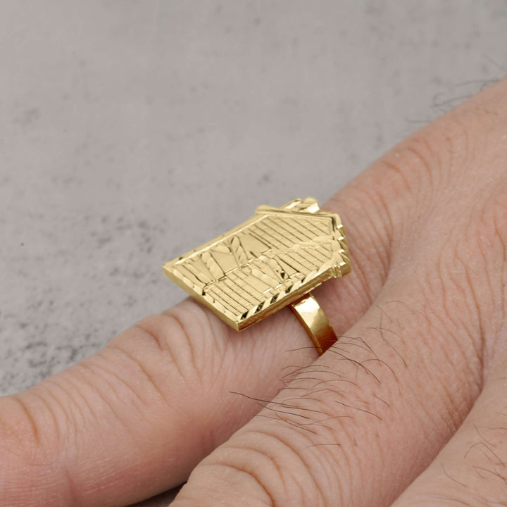A 10k gold trap house signet ring being worn on a person's pinky finger.
