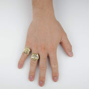 Hand wearing two 10k gold trap house signet rings on a white background.