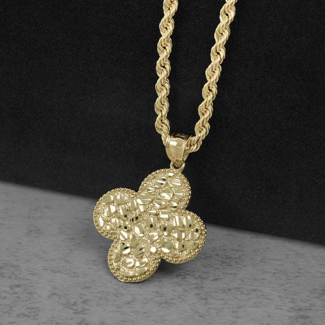 A gold-tone four-petal flower pendant necklace with a textured, beaded surface and a twisted rope chain, displayed on a split black and gray background.