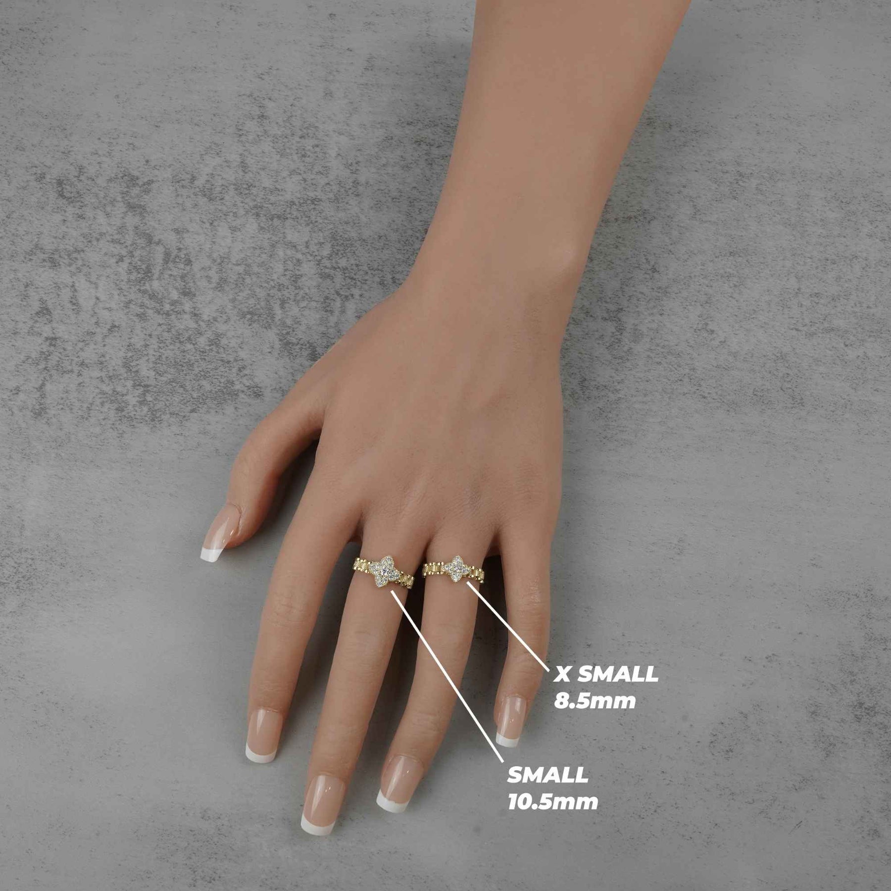 Hand wearing two 10k rings with size labels on a gray background