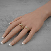 Hand wearing two 10k gold rings with Cubic Zirconia accents on a gray background