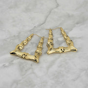 Two polished 10k yellow gold bamboo-textured square hoop earrings displayed on a marble surface.