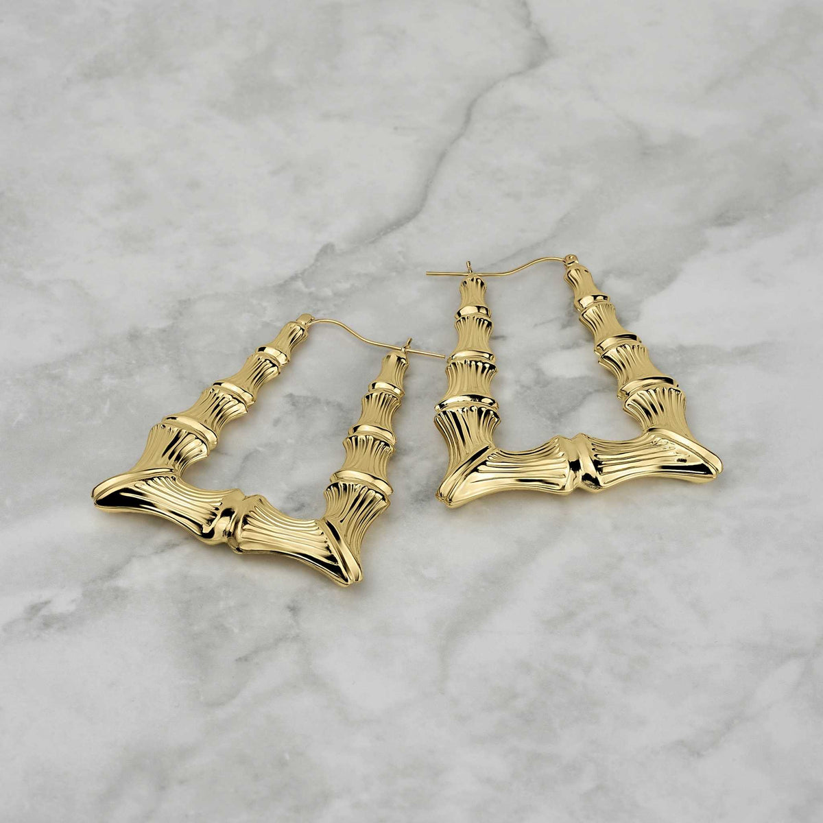 Two polished 10k yellow gold bamboo-textured square hoop earrings displayed on a marble surface.