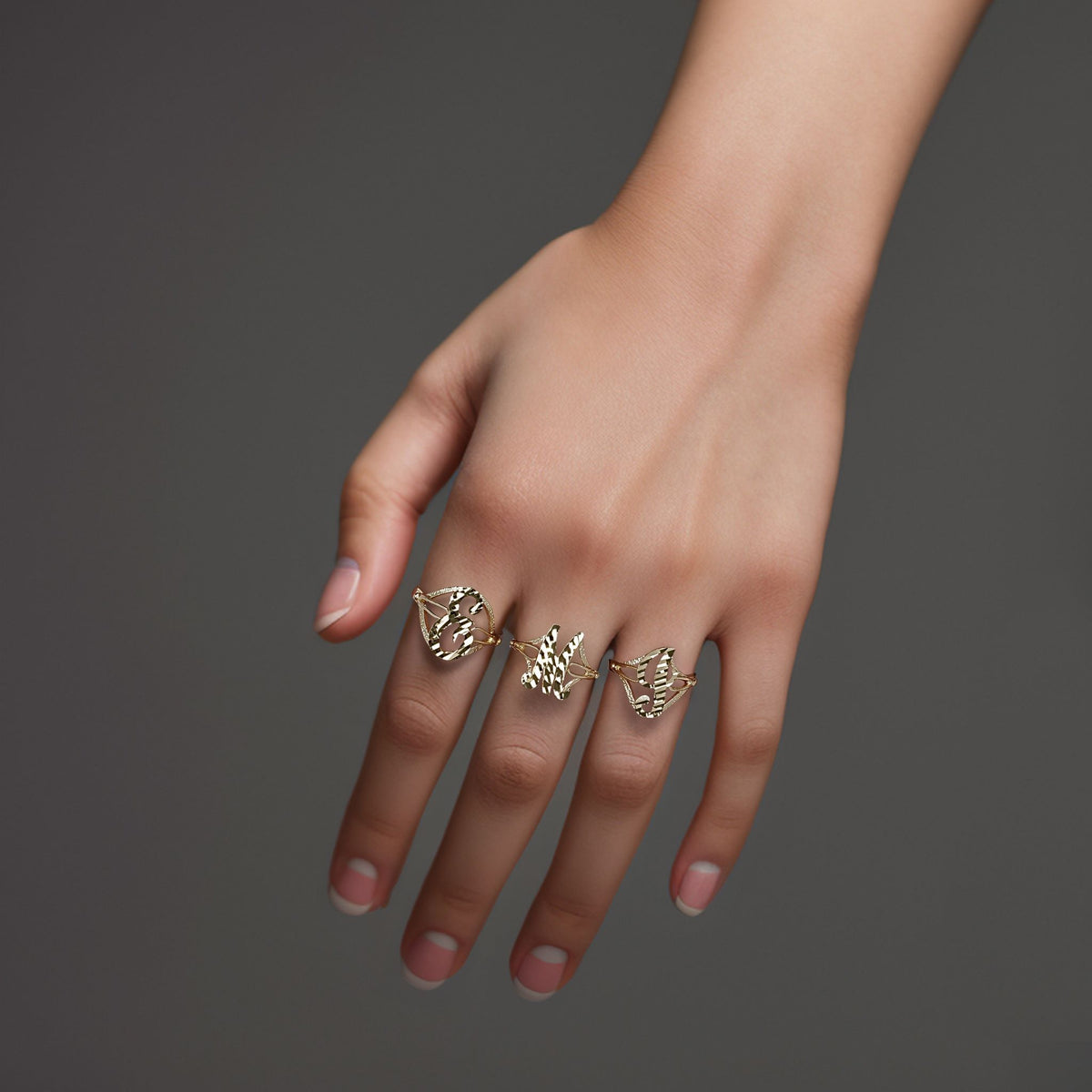 Hand wearing three 10k yellow gold vintage cursive initial rings on dark background.