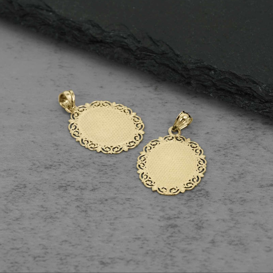 Close-up of the back of two intricate gold filigree-edged pendant charms resting on a dark-textured background.
