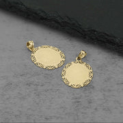 Close-up of the back of two intricate gold filigree-edged pendant charms resting on a dark-textured background.