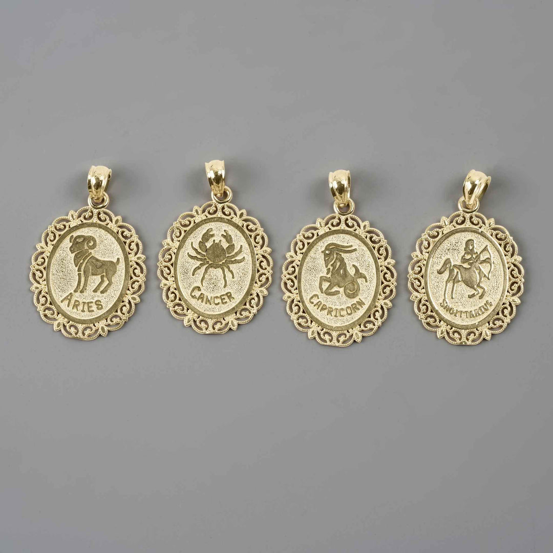 Four solid 10k yellow gold zodiac pendants featuring the Aries, Cancer, Capricorn, and Sagittarius designs against a gray backdrop.