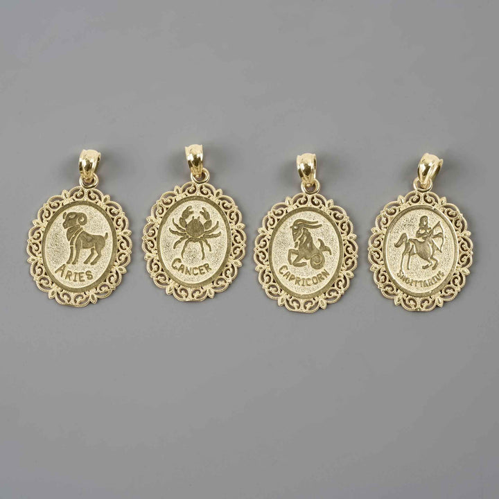 Four solid 10k yellow gold zodiac pendants featuring the Aries, Cancer, Capricorn, and Sagittarius designs against a gray backdrop.