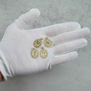 Detailed shot of Aquarius, Scorpio, Leo, and Libra gold zodiac sign pendants held on a white-gloved palm over a neutral surface.