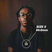 A man wearing a black t-shirt, black cap, and round glasses, wearing a gold chain necklace with a circular pendant. A white overlay circle highlights the pendant, with text reading 'SIZE 5'.