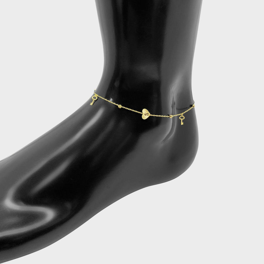10k gold heart and key charm link anklet displayed on a black mannequin foot.