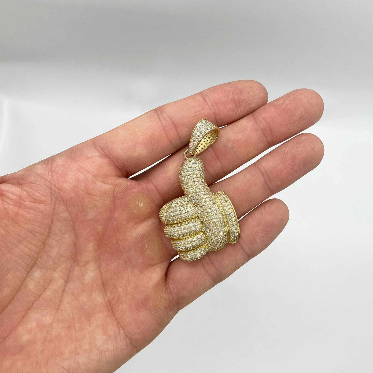 10k yellow gold iced-out thumbs up CZ pendant charm resting on an open hand