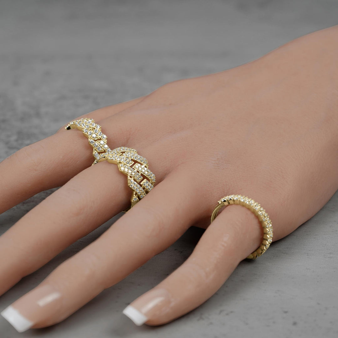 Three gold Cuban link band rings worn on a hand against gray stone.