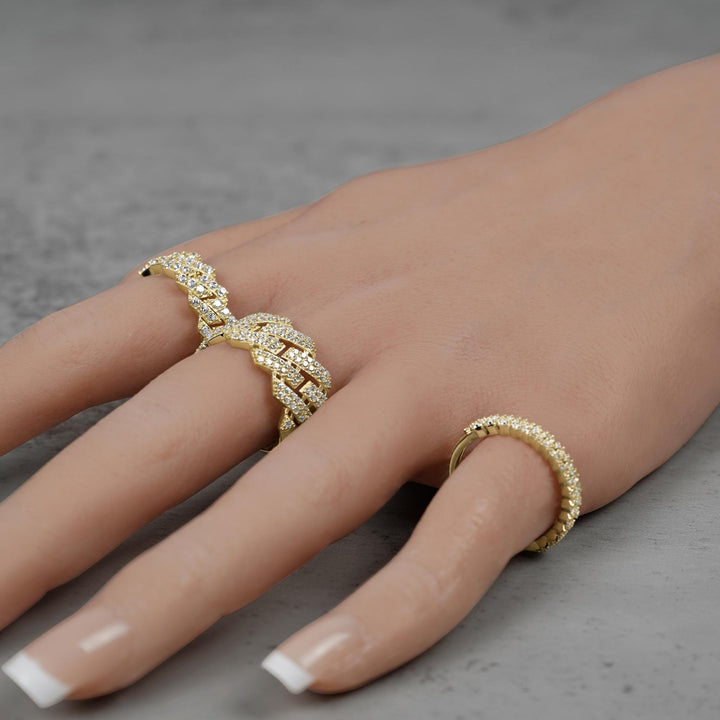 Three gold Cuban link band rings worn on a hand against gray stone.