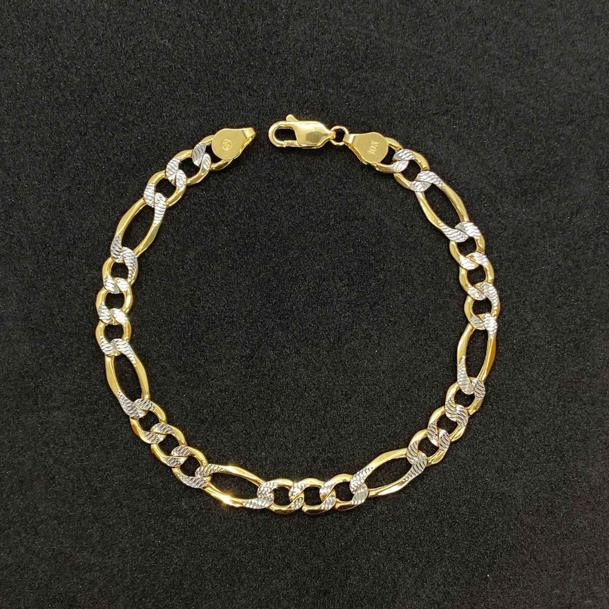 10k gold pave Figaro link chain bracelet displayed on a dark textured background.