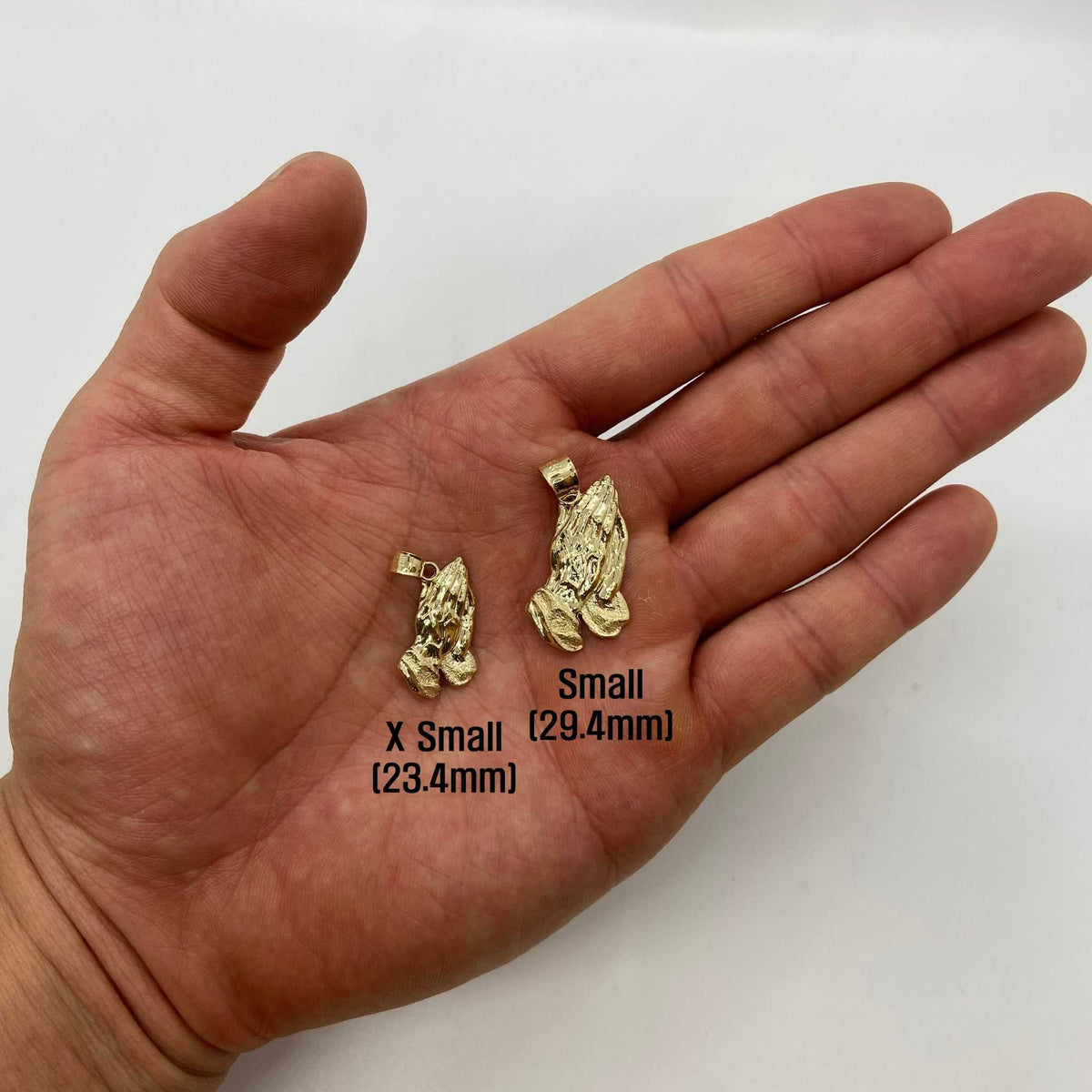 Two sizes of 10k solid gold praying hands pendants resting on an open palm