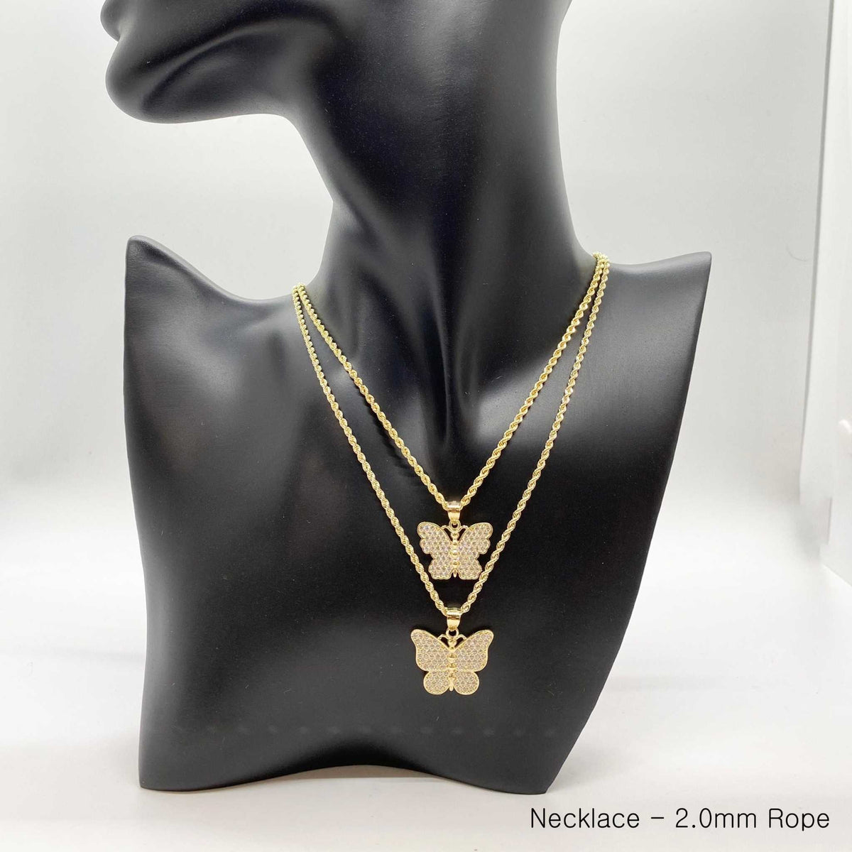 Two gold butterfly CZ pendants displayed on layered rope chain necklaces on a mannequin bust.