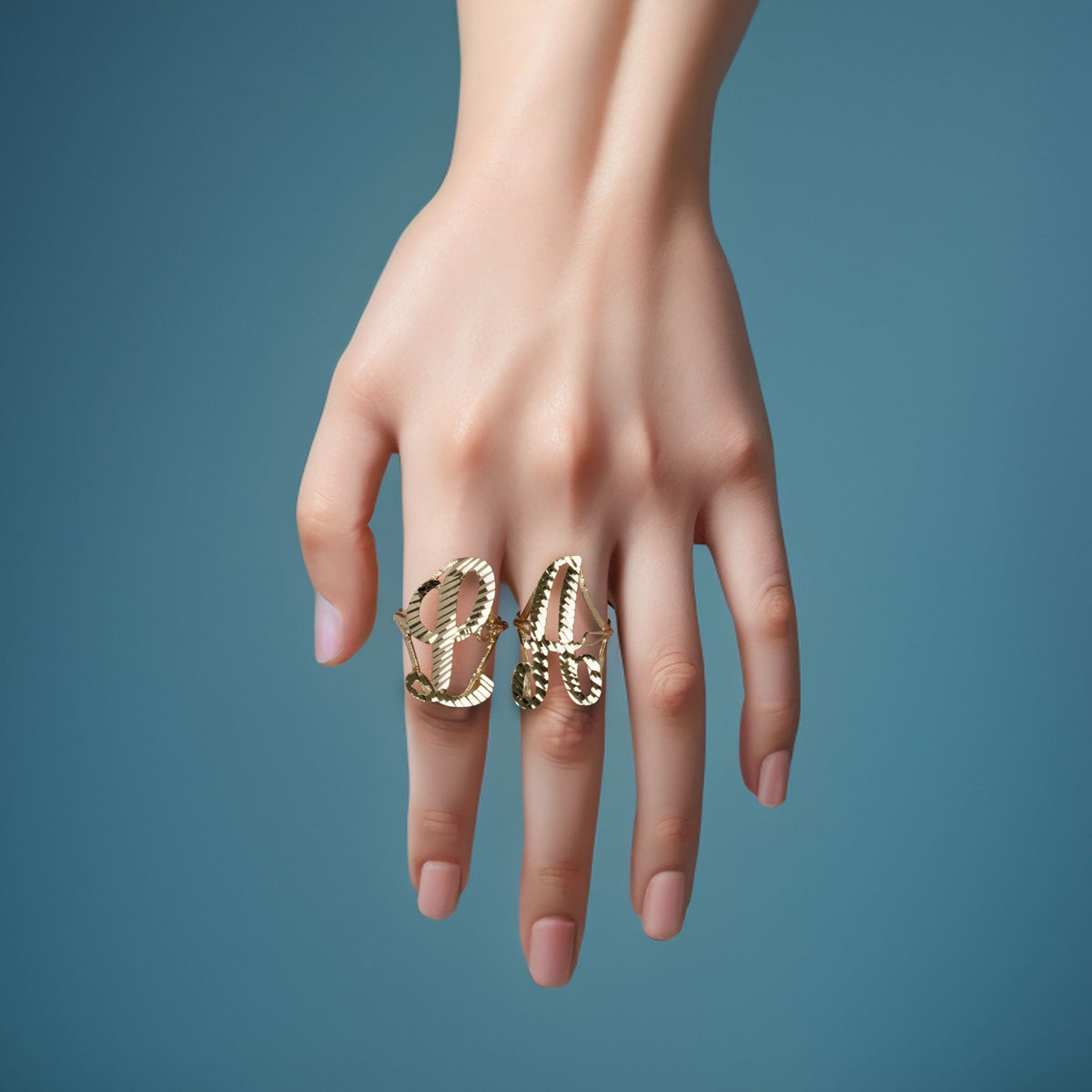 Hand wearing two 10k yellow gold large vintage cursive initial rings on blue background.