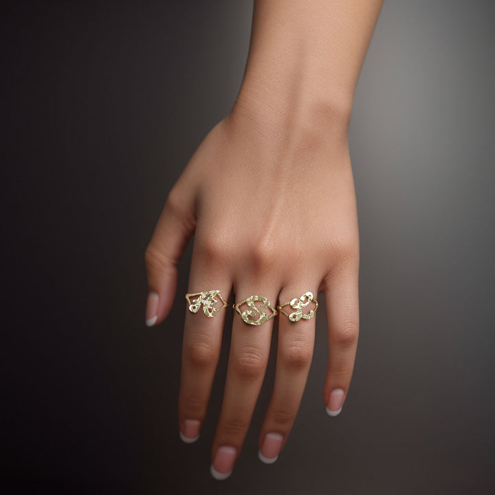 Hand wearing three 10k yellow gold vintage nugget initial rings on a dark background.