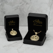 Two gold Centenario pendant necklaces displayed in open black jewelry boxes on marble.