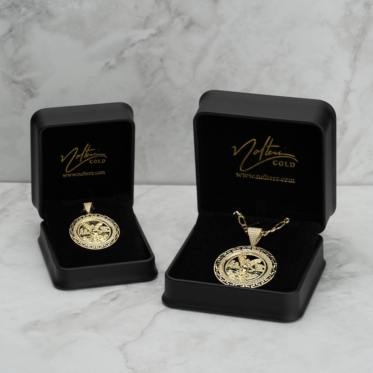 Two gold Centenario pendant necklaces displayed in open black jewelry boxes on marble.