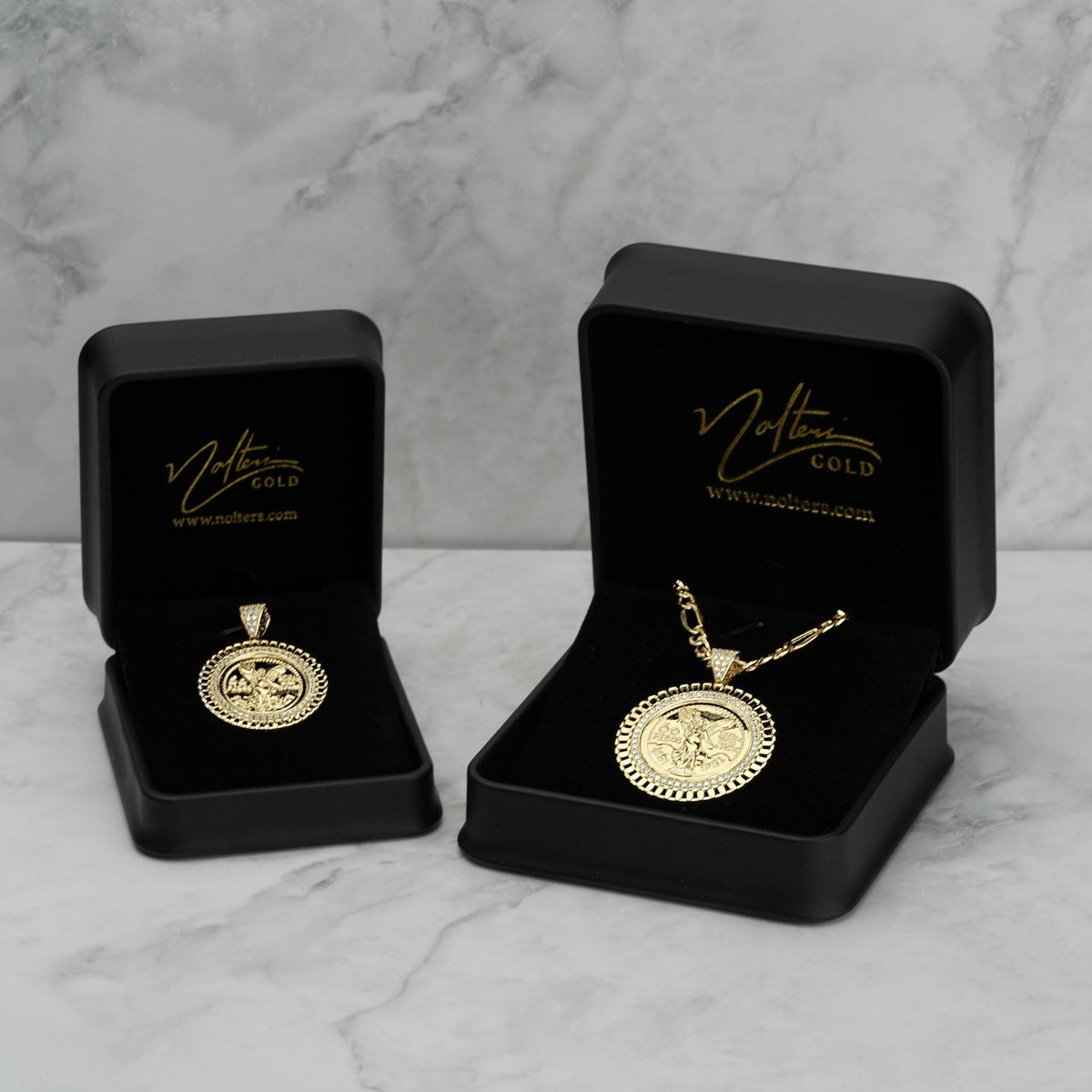 Two gold Centenario pendant necklaces displayed inside open black jewelry boxes on marble.