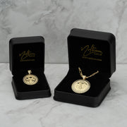 Two gold coin pendant necklaces displayed in open black jewelry boxes on marble